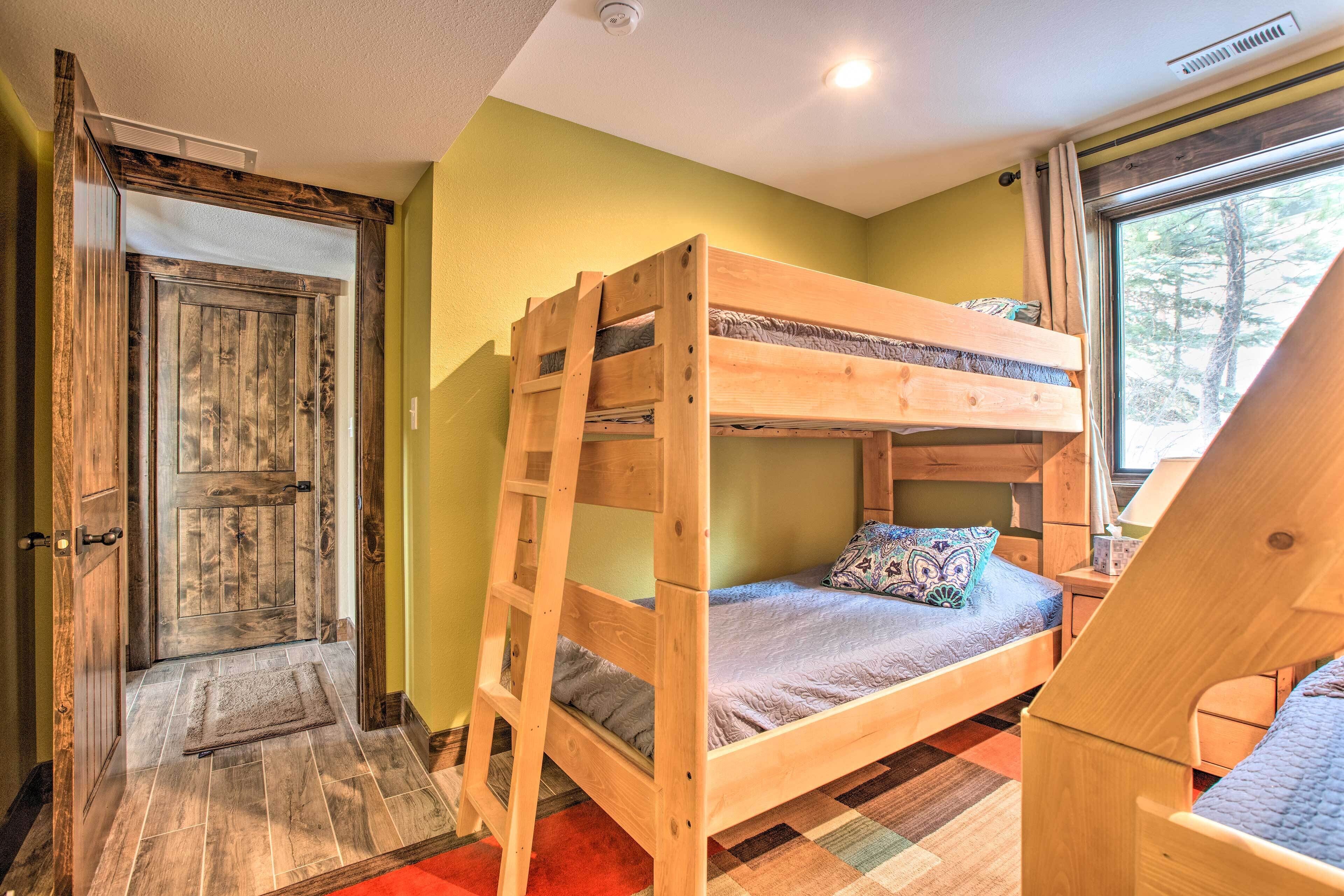 A bunk bed in a room with a wooden door, a window with a view of trees, and a red rug on the floor.
