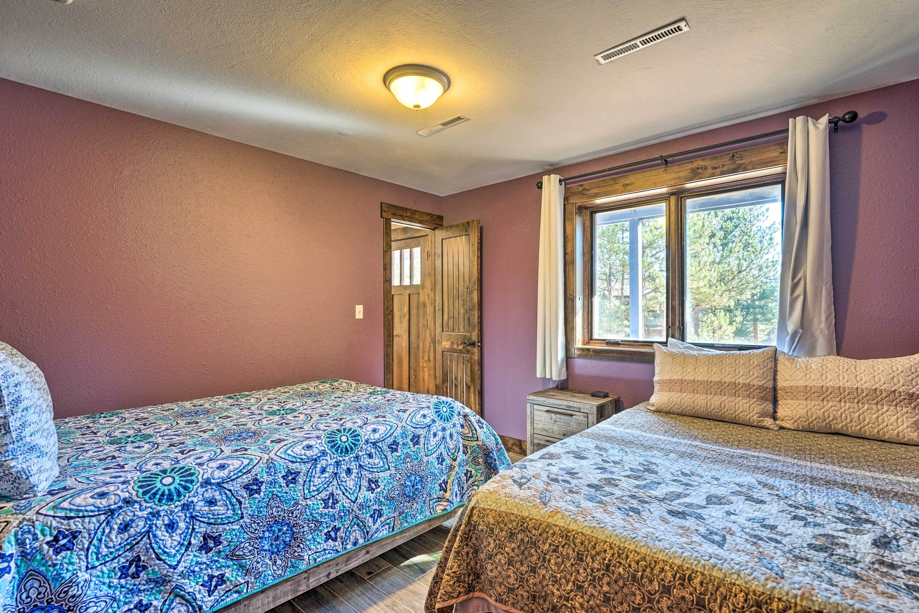 A bedroom with two beds, a window with curtains, a wooden door, and a ceiling light.
