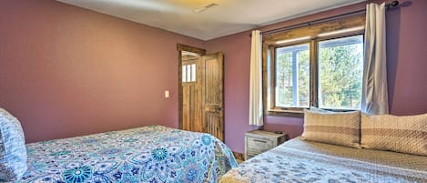 A bedroom with two beds, a window with curtains, a wooden door, and a ceiling light.