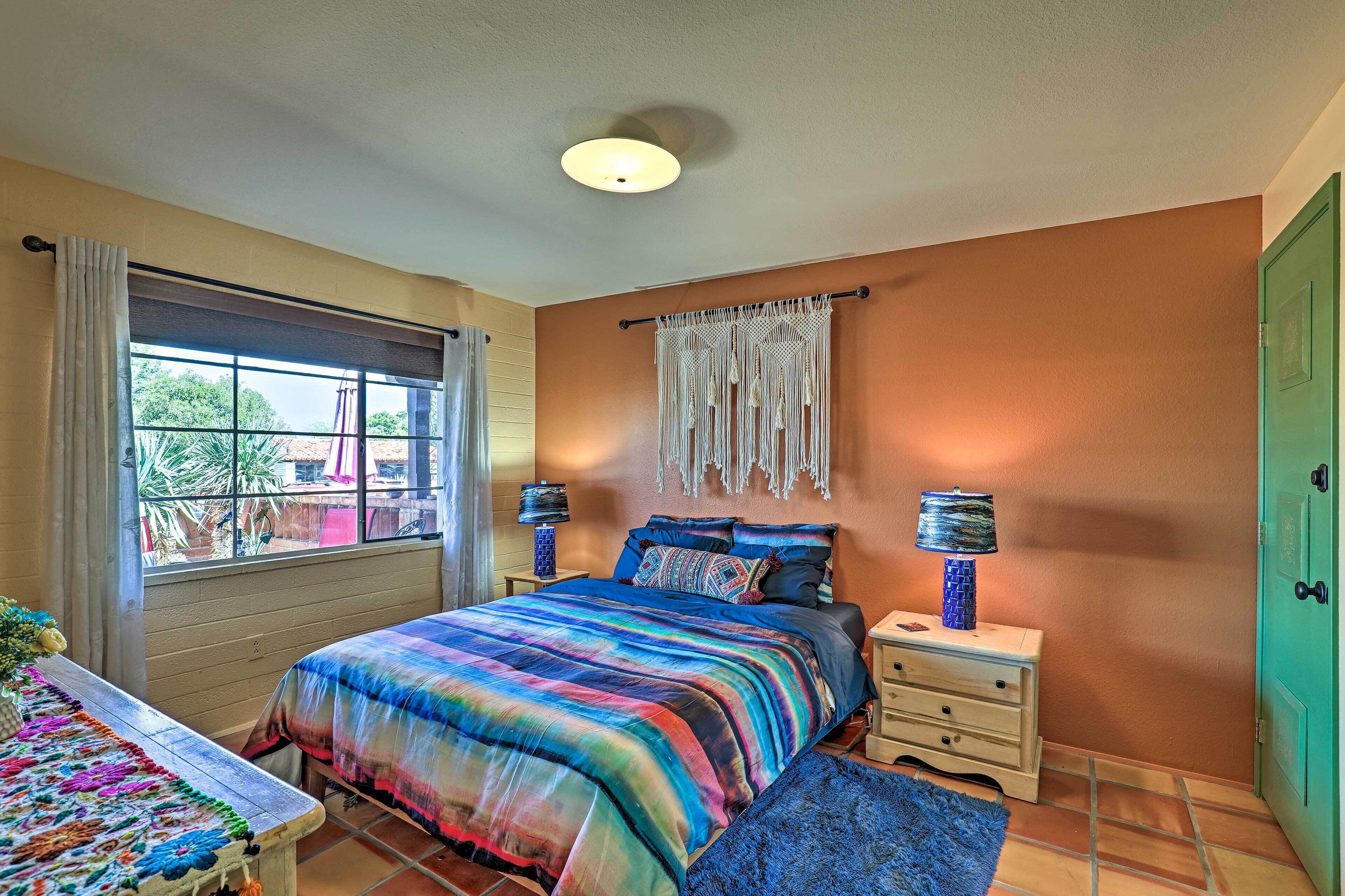 A bedroom with a large bed, a nightstand with lamps, a window with curtains, and a green door.