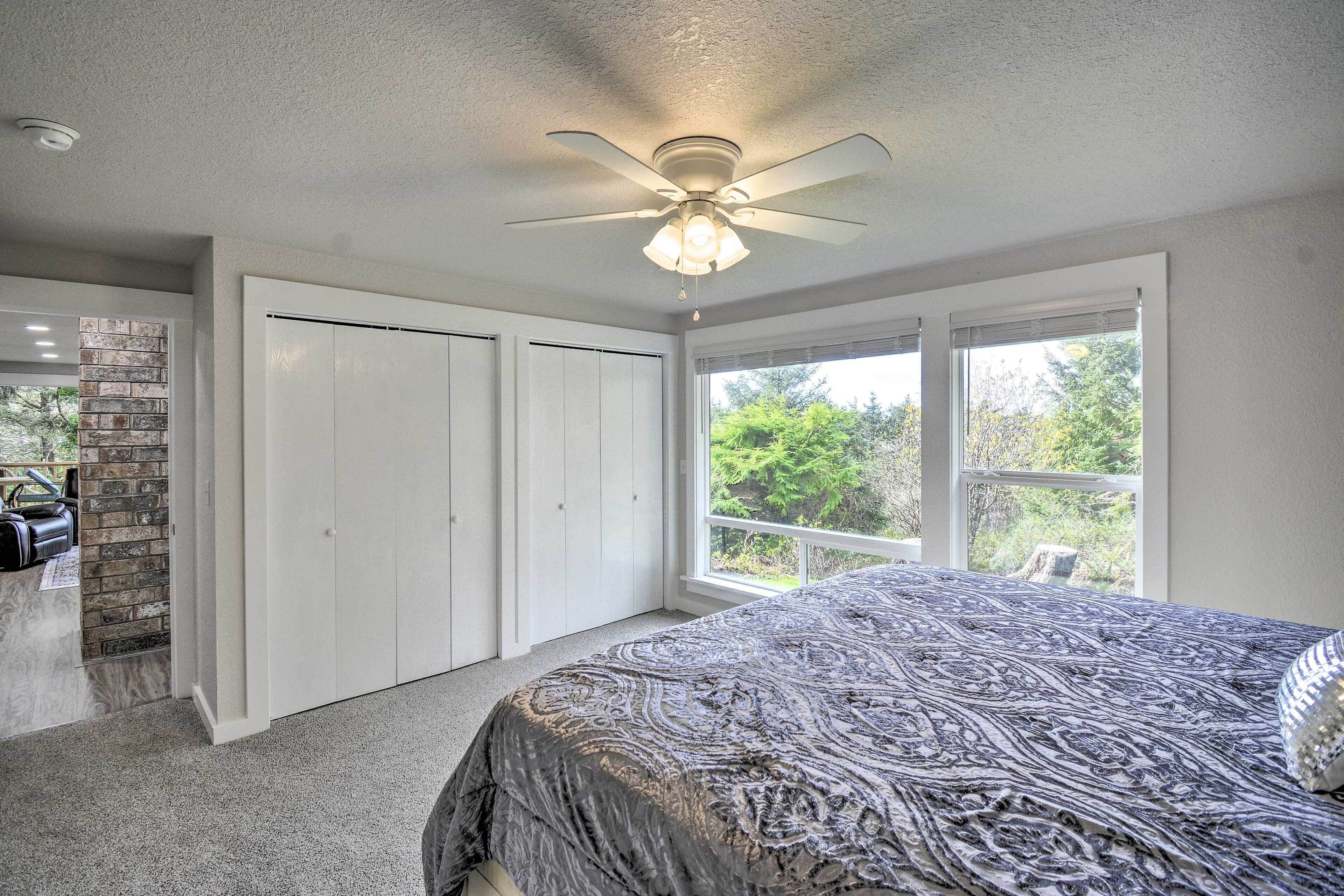 A bedroom with a bed, a ceiling fan, a window with a view of greenery, and a closet.
