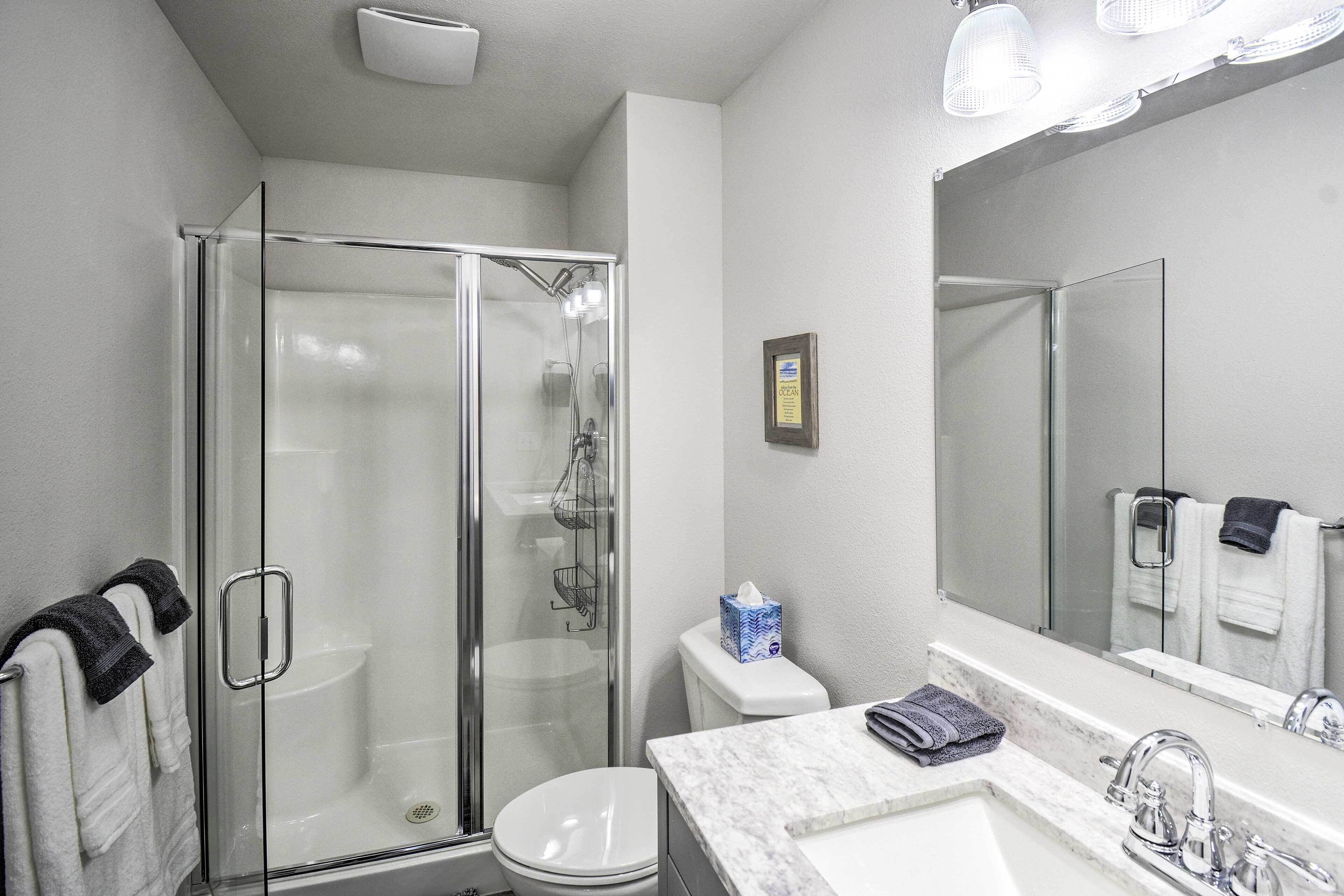 A bathroom with a glass-enclosed shower, a white toilet, a marble sink, and a large mirror.