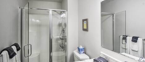 A bathroom with a glass-enclosed shower, a white toilet, a marble sink, and a large mirror.