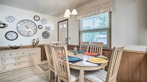 A dining room with a round table, wooden chairs, and a variety of clocks on the wall.