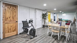 A room with a treadmill, a dining table with chairs, a pool table, and a door with a wooden panel.