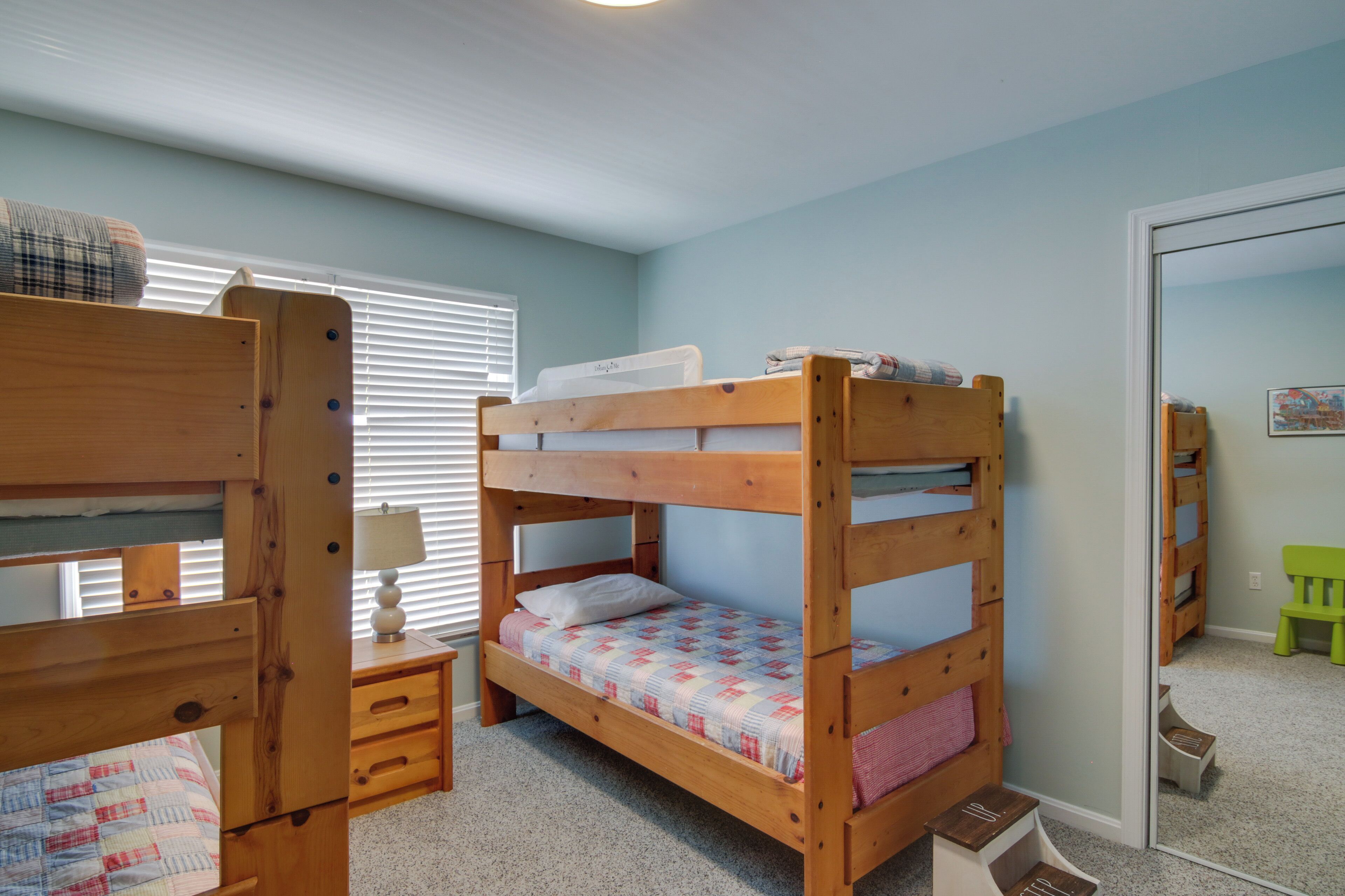 A bunk bed room with a wooden desk and chair, a lamp, and a window with blinds.