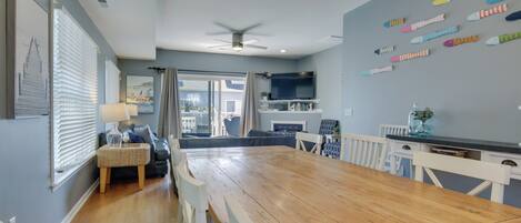 A spacious living room with a wooden dining table, a sofa, and a TV mounted on the wall.