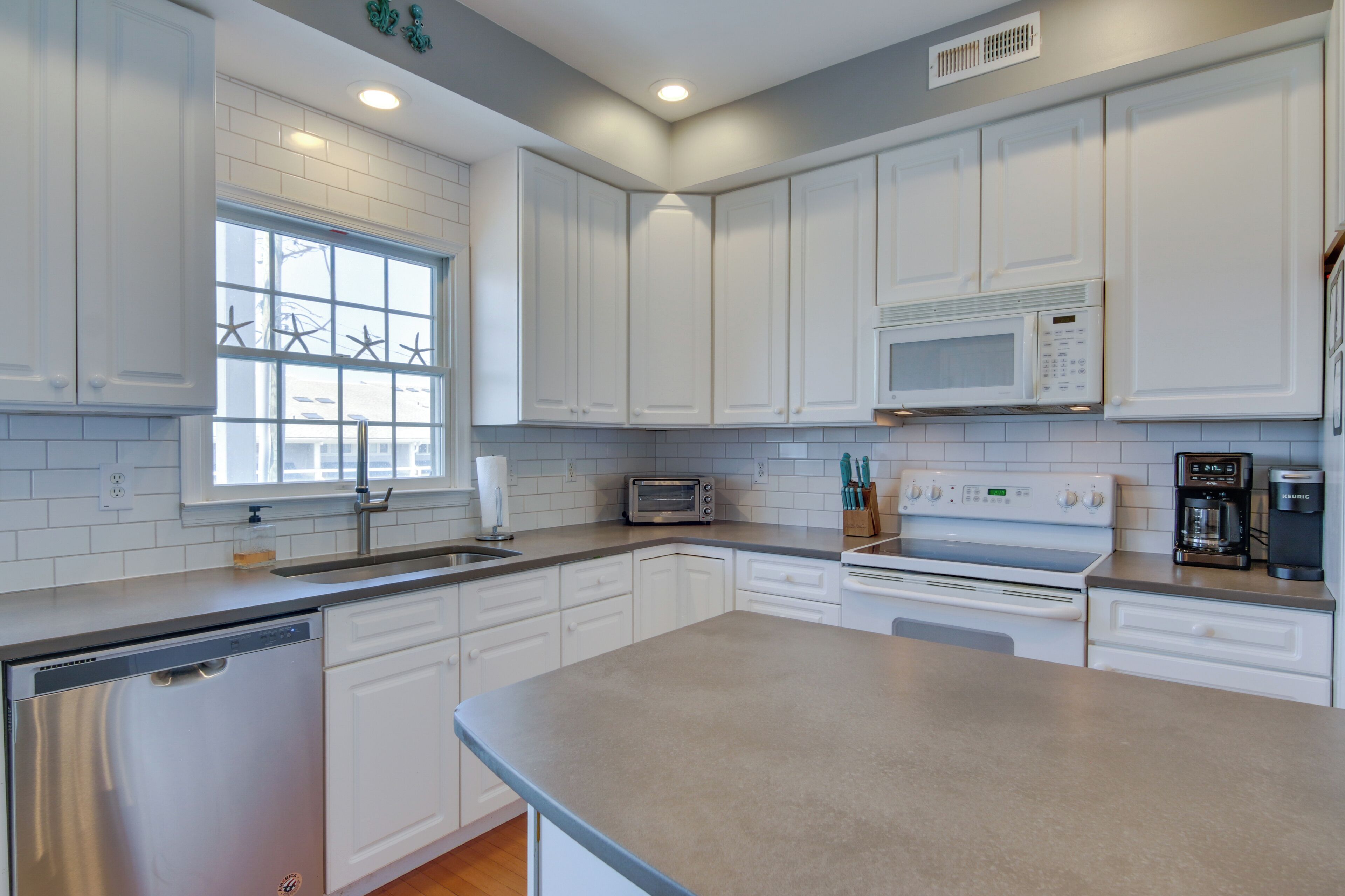 A modern kitchen with white cabinets, a dishwasher, a microwave, a toaster, and a coffee maker.