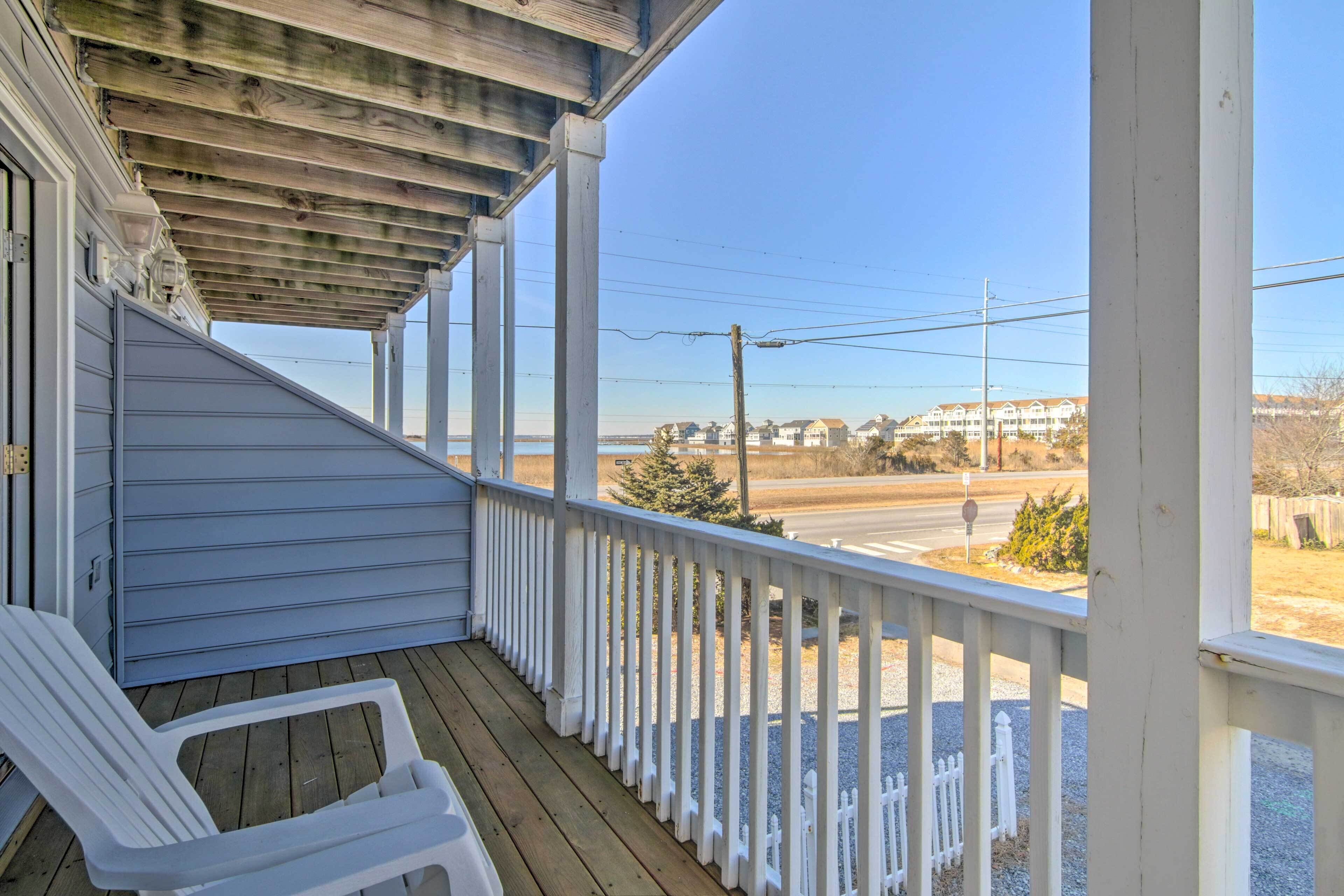 A wooden porch with white railings, a clear view of the road, and a white fence in the background.