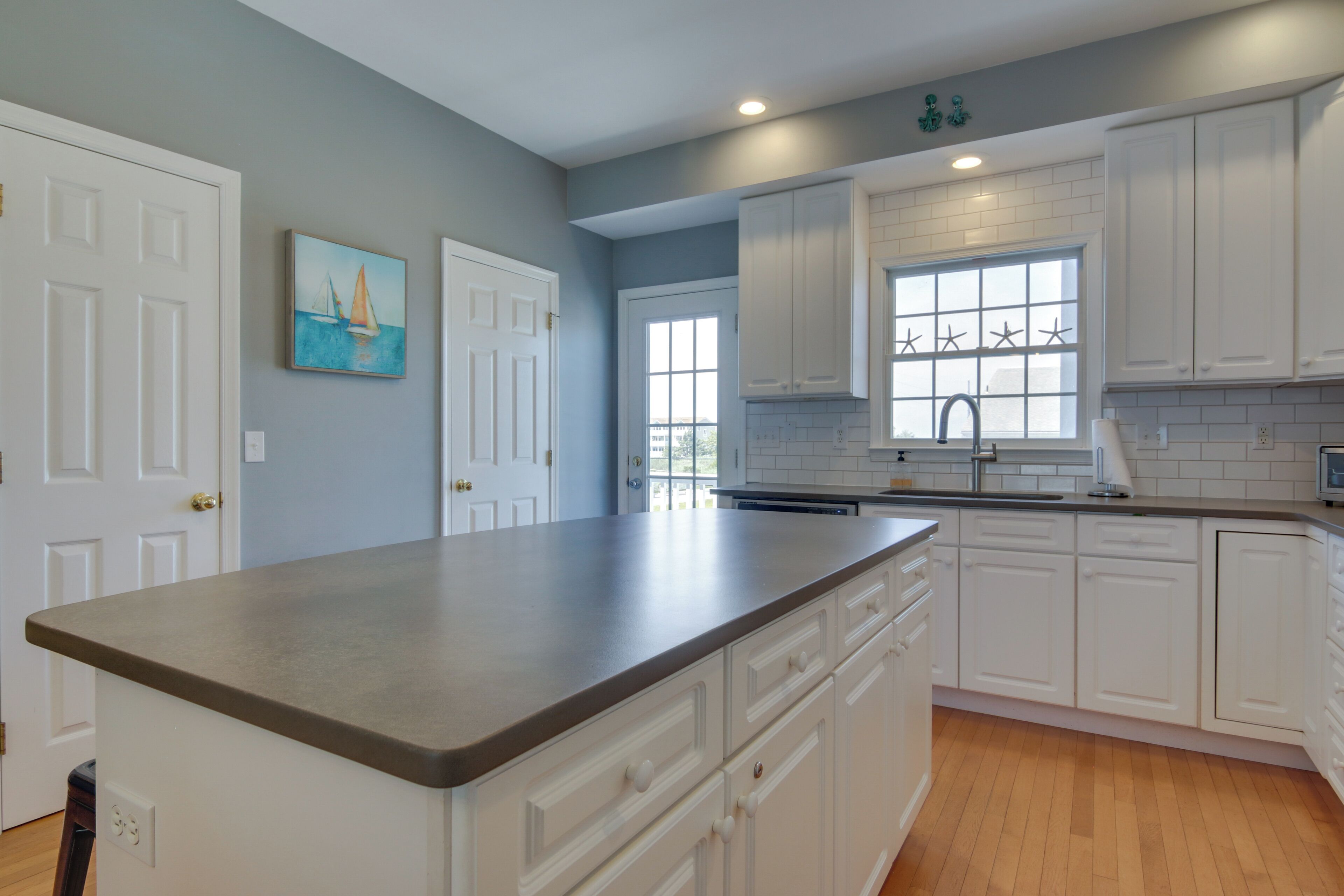 A kitchen with white cabinets, a large island, and a window with starfish decorations.