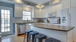 A modern kitchen with white cabinets, a large island with stools, a microwave, and a refrigerator. - Bay-view Retreat w/ 5 Balconies in Bethany Beach! (Bethany Beach)