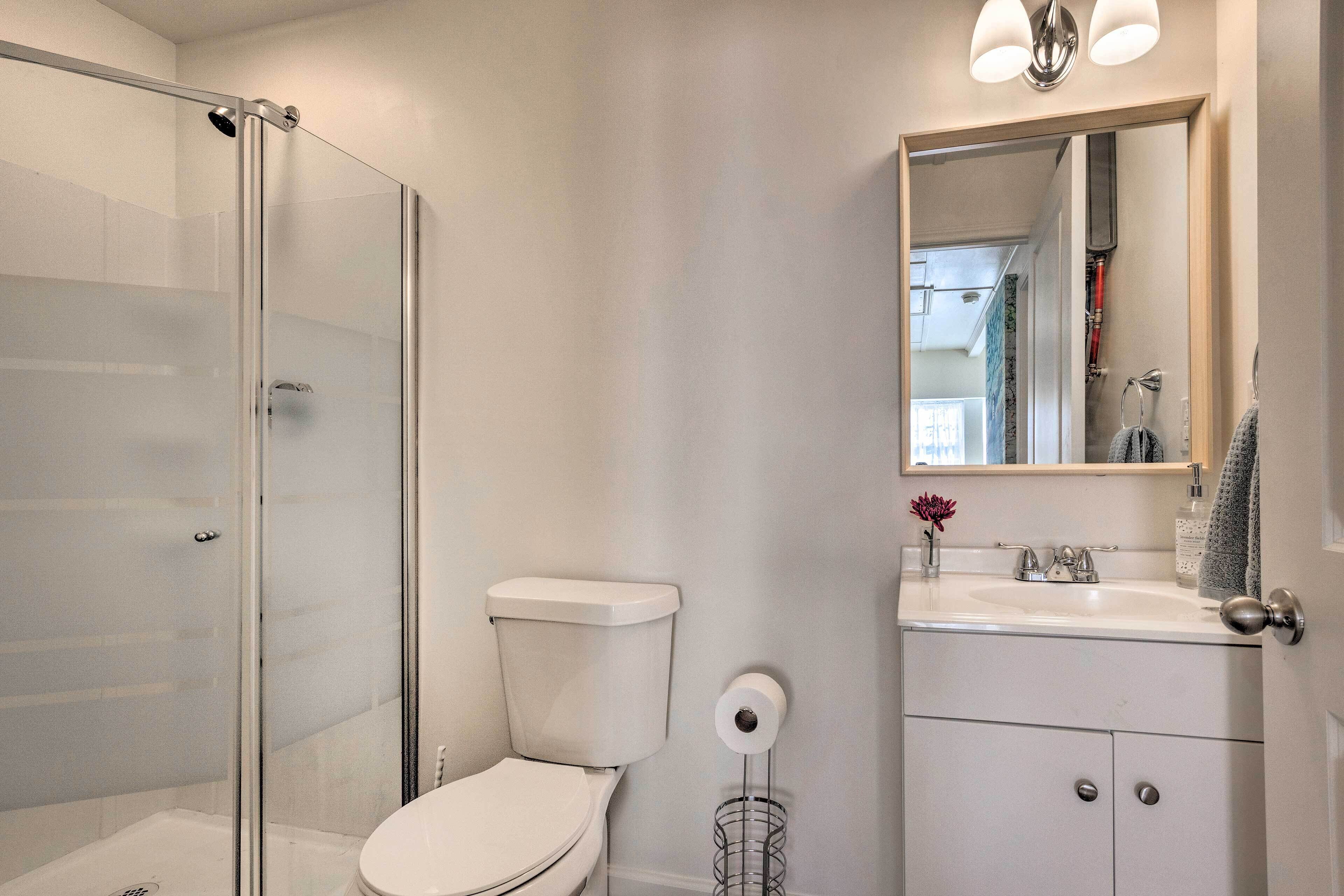 A modern bathroom with a glass shower enclosure, a white toilet, a sink with a mirror above it, and a small vase with a flower.