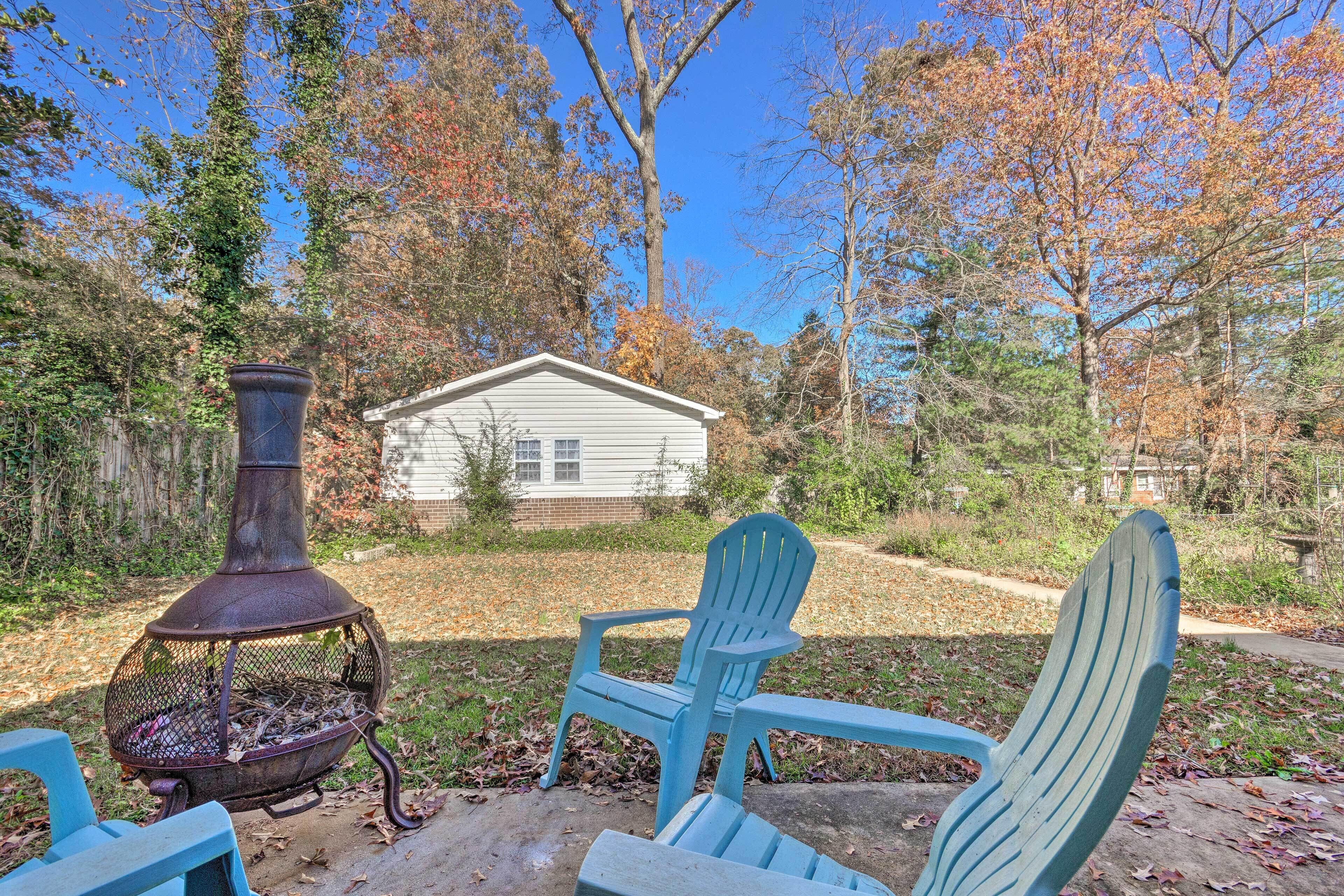 A backyard with a metal fire pit, two Adirondack chairs, and a house in the background.