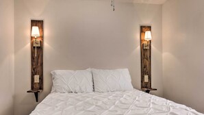A bed with a white quilted cover, flanked by two wall-mounted nightstands with lamps. - Claires Cottage ~ 4 Mi to Downtown Greenville! (Greenville)