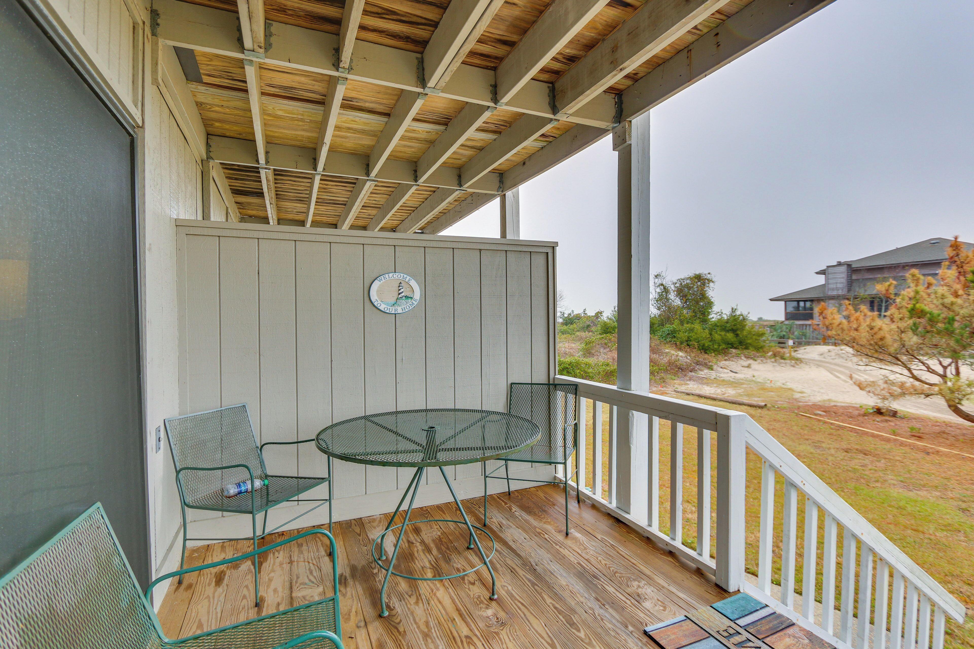 A covered outdoor area with a table and two chairs, a wooden deck, and a white railing.