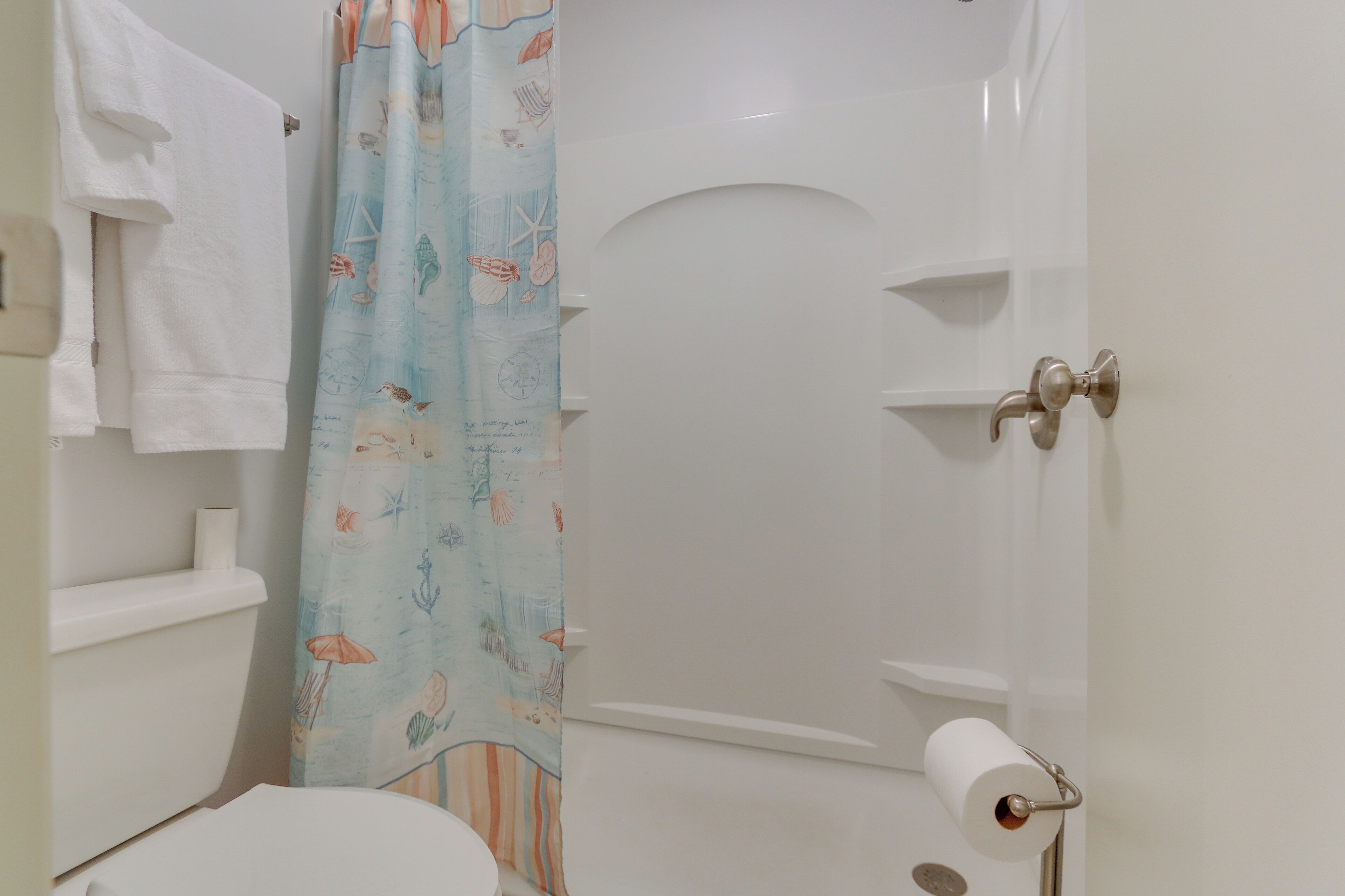 A bathroom with a toilet, a towel rack, a shower curtain with sea creatures, and a toilet paper holder.