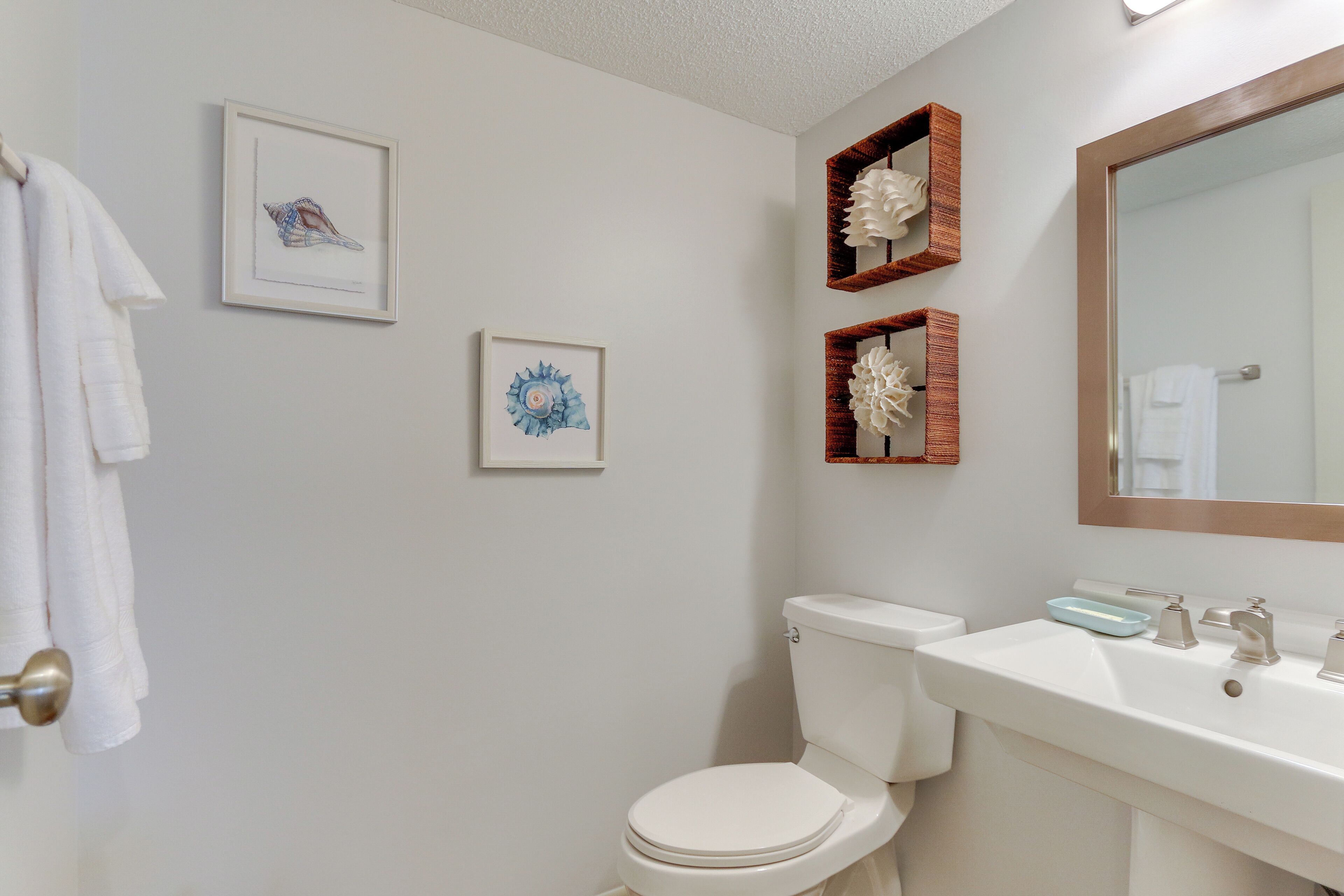 A bathroom with a toilet, sink, and framed artwork on the wall.