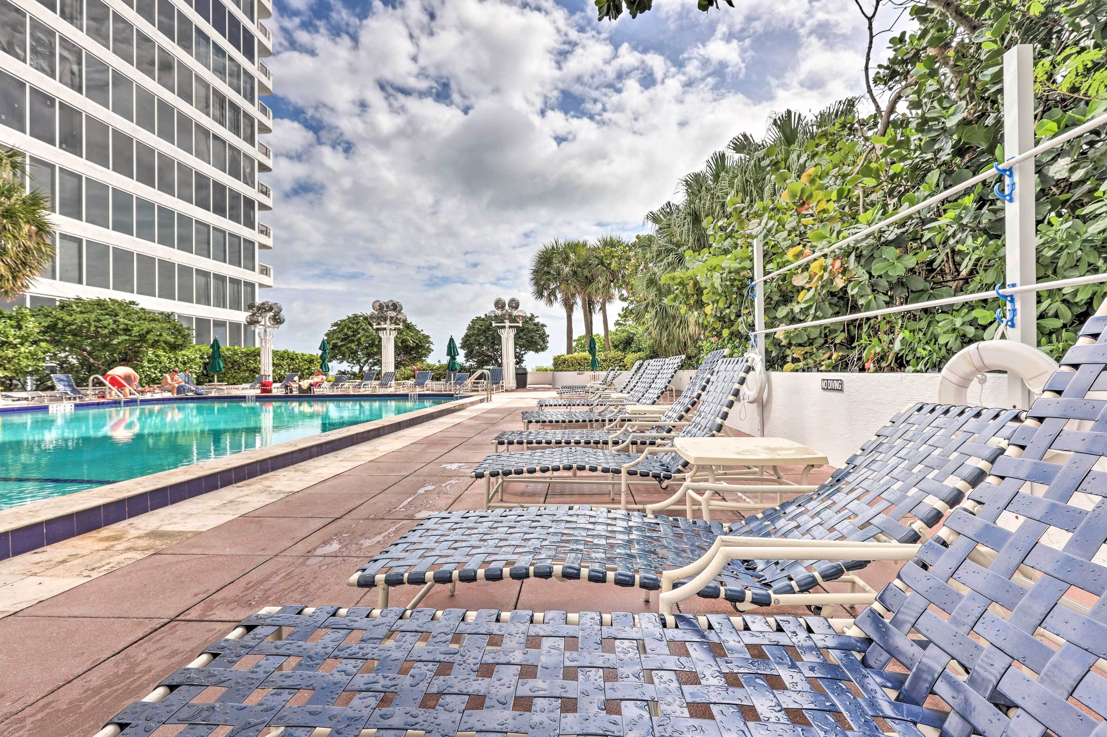 A poolside area with lounge chairs, a swimming pool, and a building in the background.