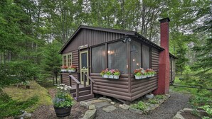 A rustic cabin with a chimney, wooden exterior, and flower boxes on the windows. - 'sprucewold' Boothbay Harbor Cottage w/ Deck (Boothbay Harbor)