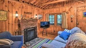 A cozy cabin interior with a fireplace, a television on a stand, and a comfortable seating area with a striped rug. - 'sprucewold' Boothbay Harbor Cottage w/ Deck (Boothbay Harbor)
