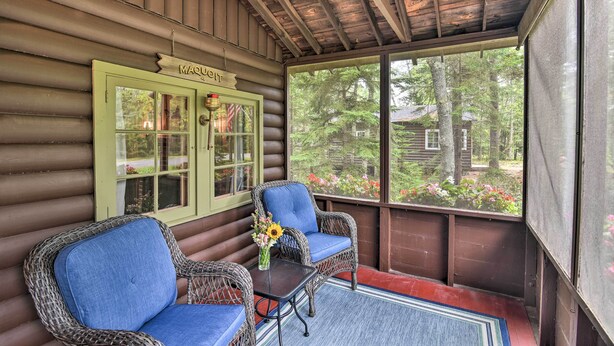 A log cabin with a porch featuring wicker chairs and a table with a vase of flowers. - 'sprucewold' Boothbay Harbor Cottage w/ Deck (Boothbay Harbor)