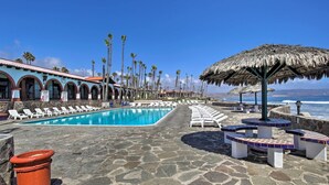 A pool area with lounge chairs and umbrellas, a stone pathway, and a building with arched windows. - Rosarito Beach Home in Las Gaviotas w/ Ocean Views (Playas de Rosarito)