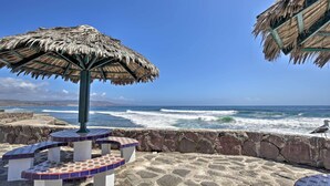A beachside patio with a thatched umbrella, stone seating, and a view of the ocean. - Rosarito Beach Home in Las Gaviotas w/ Ocean Views (Playas de Rosarito)