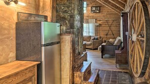 A rustic cabin interior with a stone wall, wooden beams, a large wooden wheel, and a cozy seating area. - Peaceful Log Cabin Escape Near Table Rock Lake! (Golden)