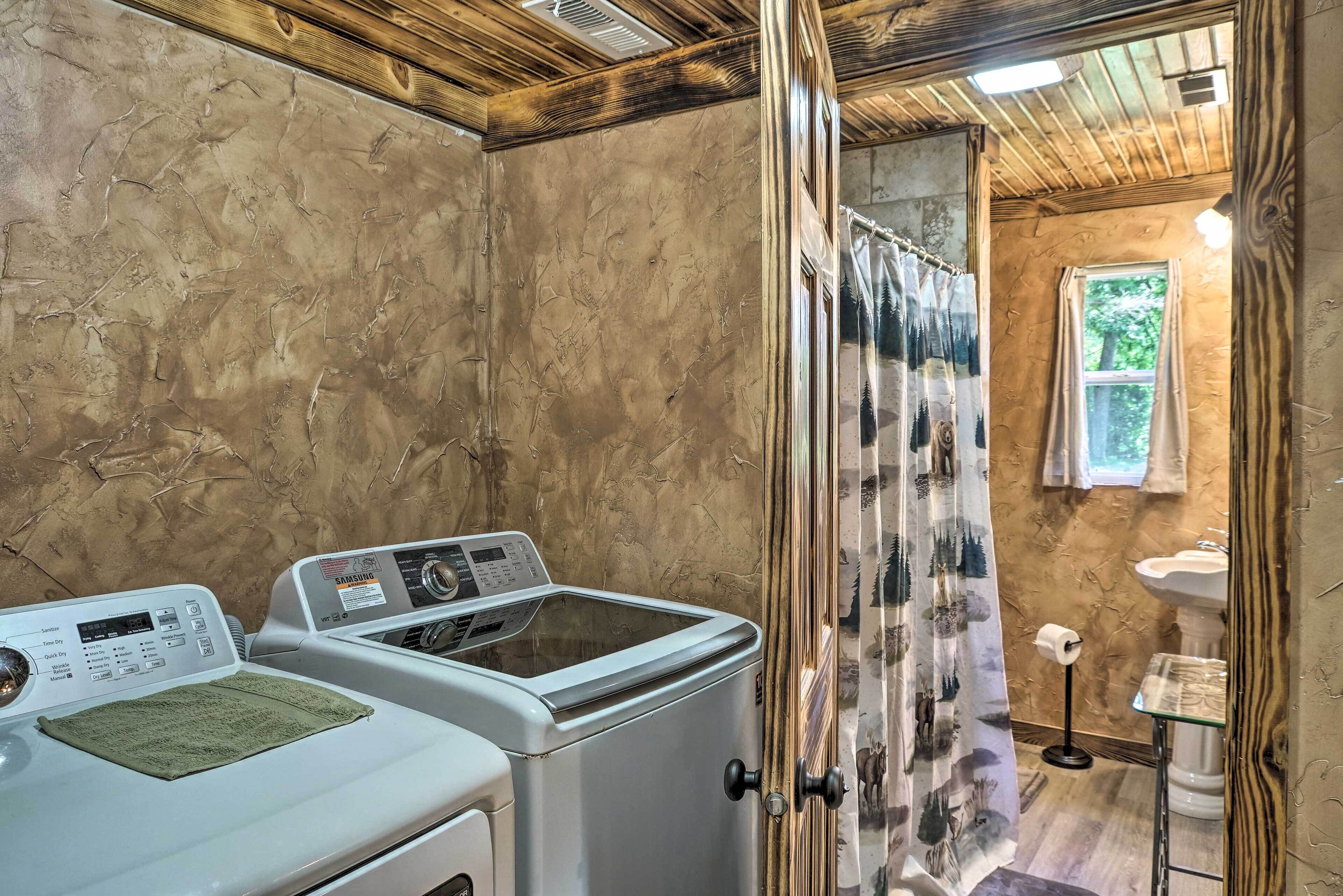 A laundry room with a washing machine and dryer, a window with a view of greenery, and a bathroom with a sink and toilet.