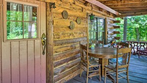 A rustic wooden cabin with a porch, a dining table with chairs, and a window overlooking greenery. - Peaceful Log Cabin Escape Near Table Rock Lake! (Golden)