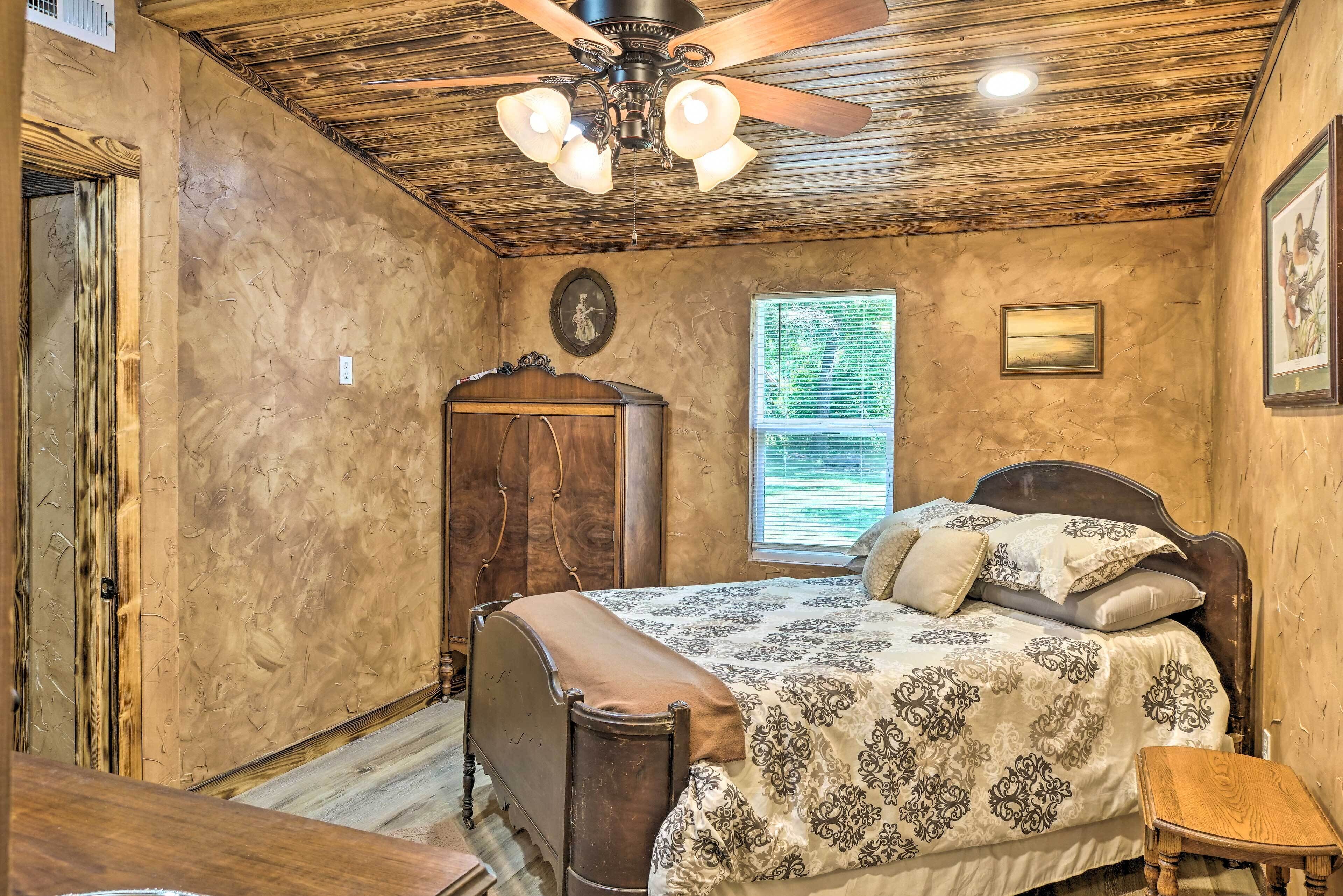 A bedroom with a wooden ceiling, a bed with patterned bedding, a wooden nightstand, and a window with blinds.