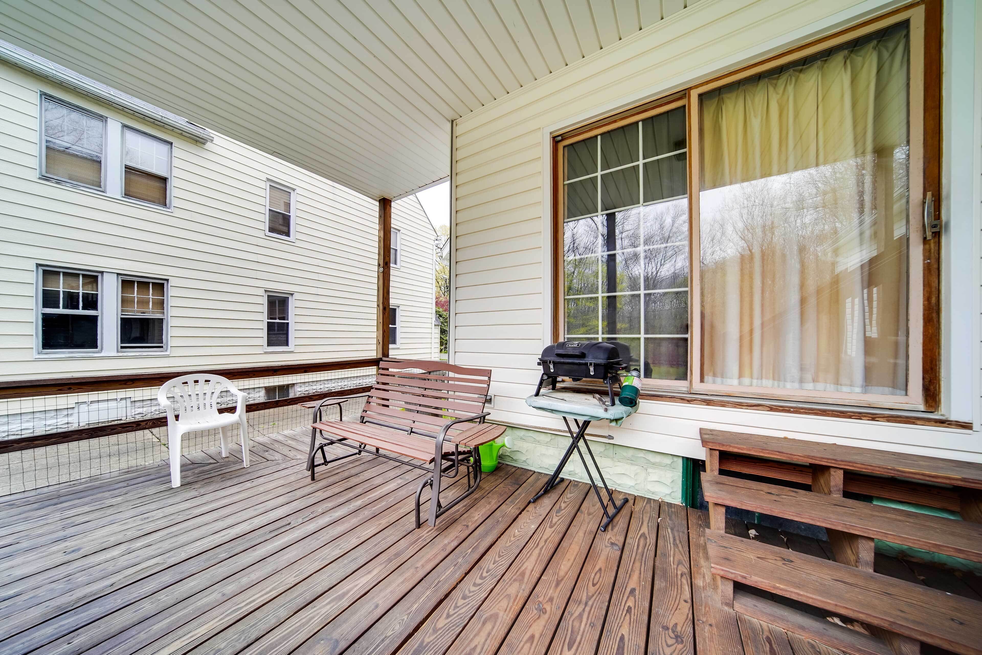 A covered porch with a wooden bench, a grill, and a white plastic chair.