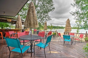 An outdoor seating area with tables and chairs, a wooden deck, and a view of the water. - Leisurely Lake Retreat: Boat Rentals & Fishing! (Dent)