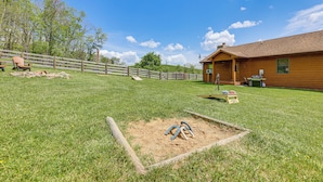 A fenced outdoor area with a wooden building, a sandbox, and a wooden bench. - Fish, Hike, Hunt: Secluded Cabin in Doe Hill! (Doe Hill)