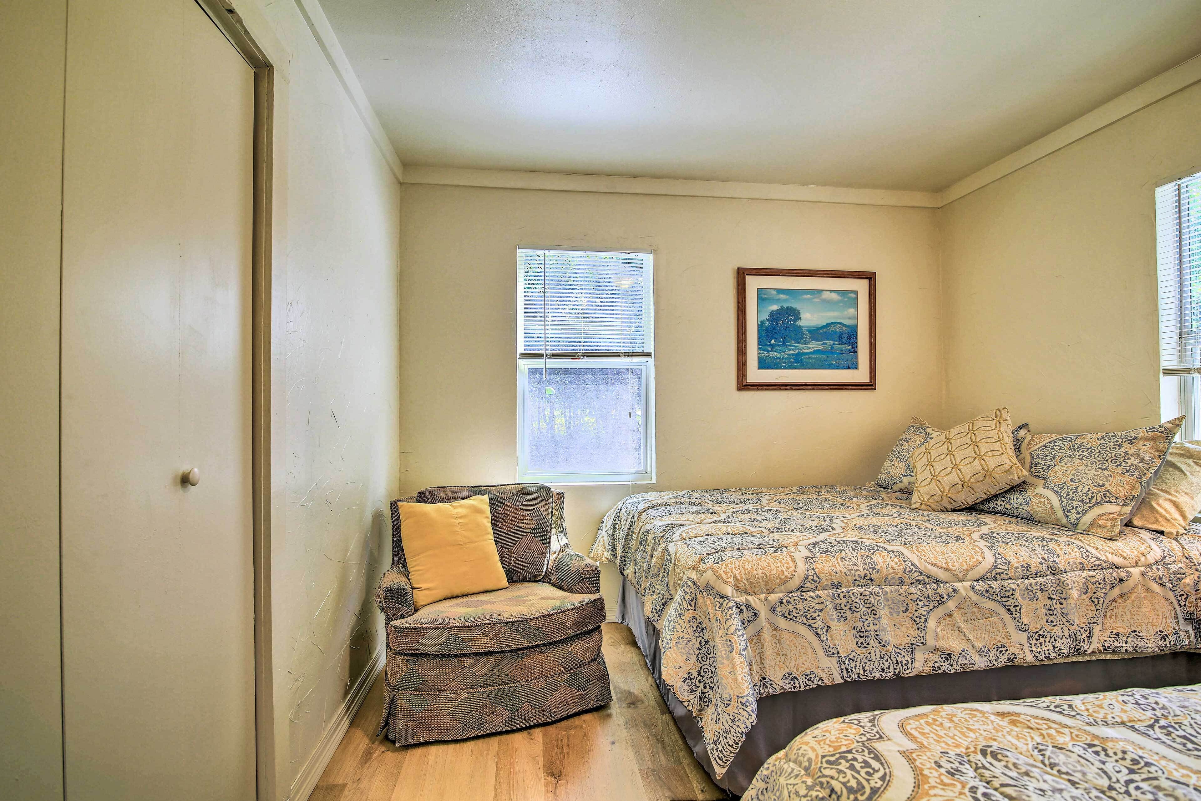 Un dormitorio con cama, una silla, un ventanal y un cuadro en la pared.