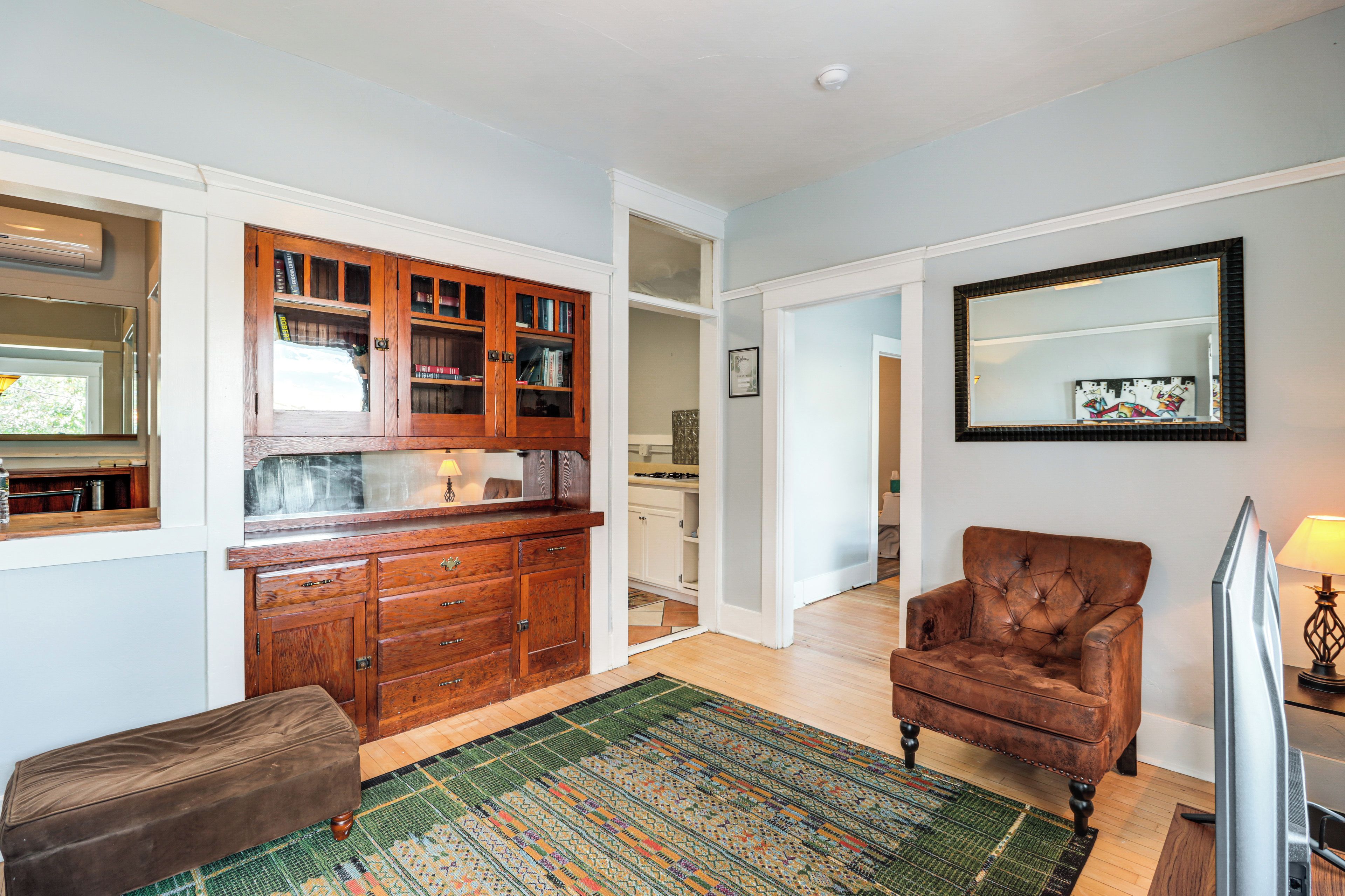 A spacious living area with a wooden cabinet, a brown leather armchair, a patterned rug, and a flat-screen TV.