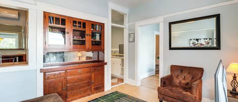 Un salón amplio con un mueble de madera, un sillón de cuero marrón, una alfombra estampada y un televisor de pantalla plana.
