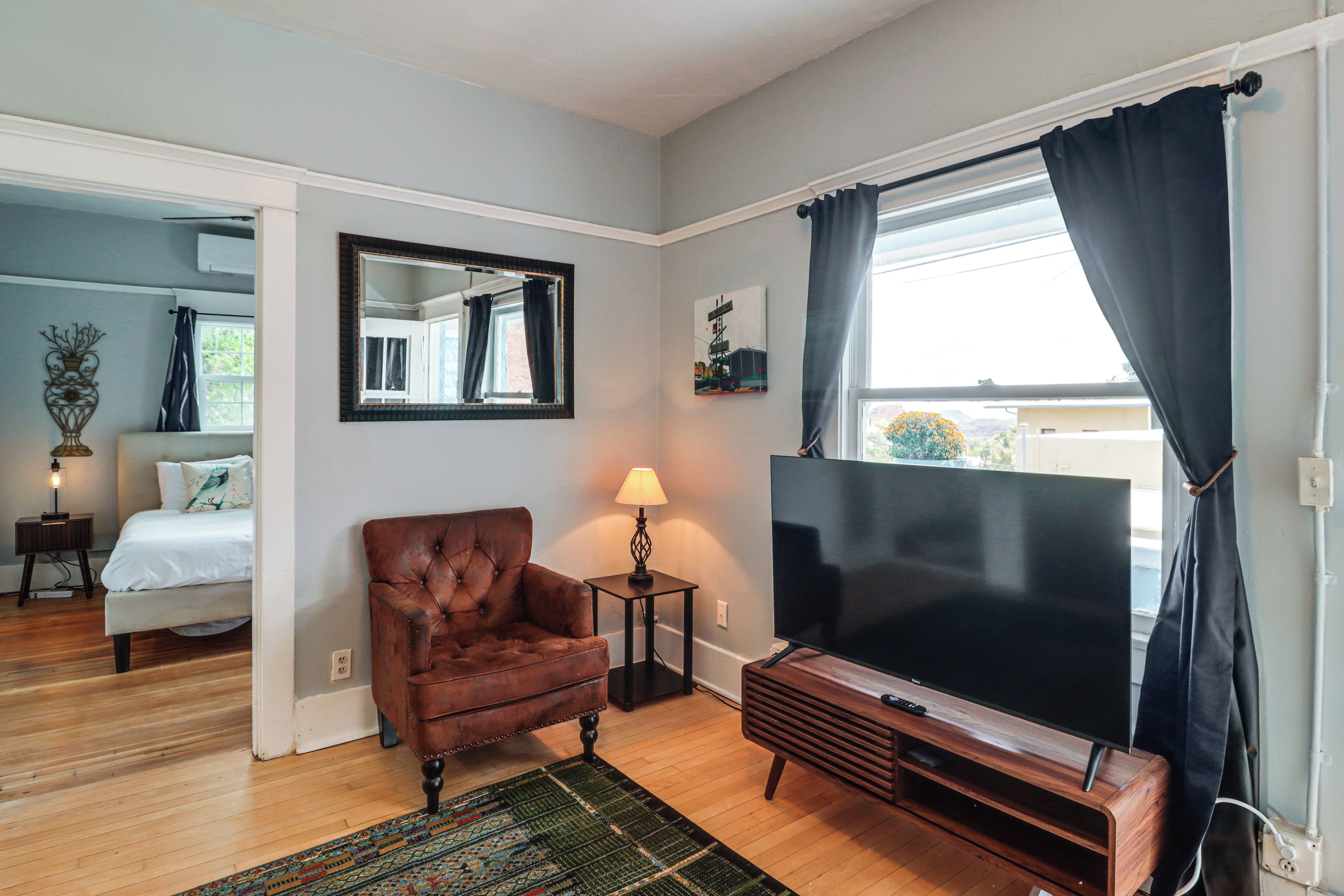 A room with a bed, a leather armchair, a TV, and a large window with curtains.