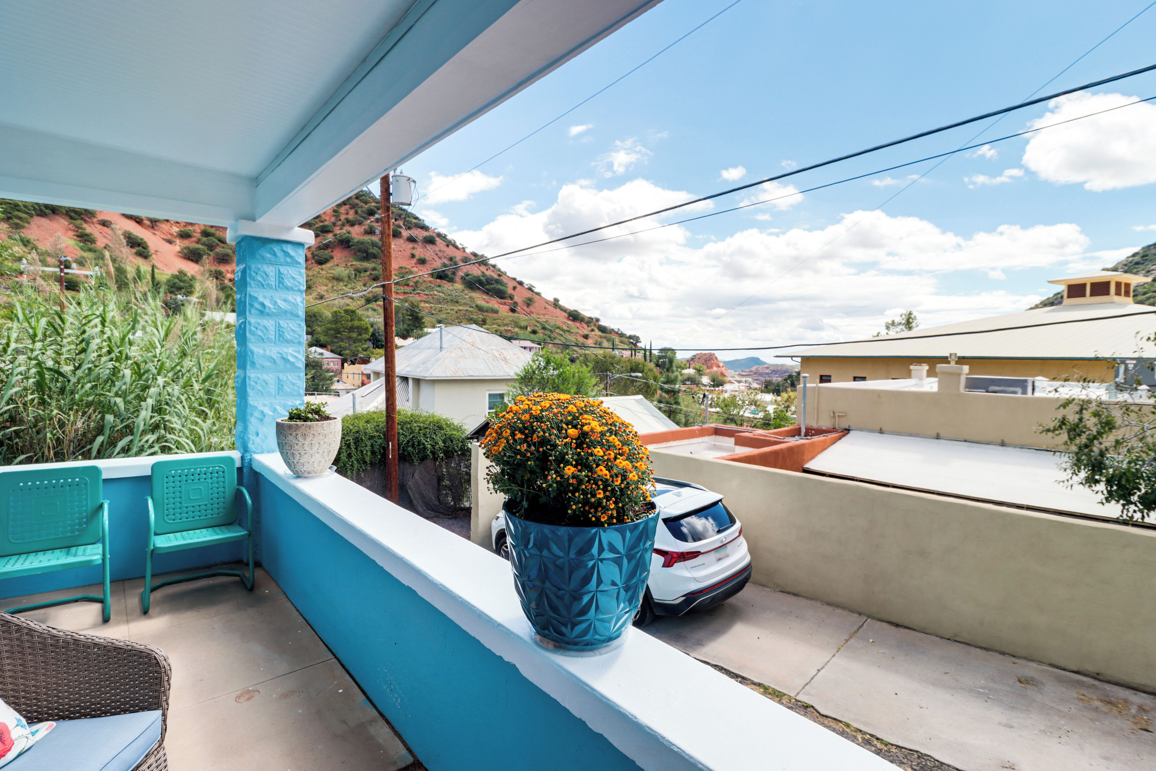 A balcony with a view of a hilly landscape, a white car, and a blue chair.