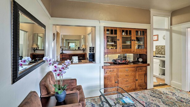 A spacious living room with a brown leather sofa, a coffee table, and a vase of flowers. There is a wooden cabinet with glass doors and a mirror on the wall. - 'St Patrick' Apartment in the Heart of Bisbee (Bisbee)