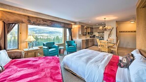 Een hotelkamer met twee bedden, een bureau, een stoel, uitzicht op de bergen, een kroonluchter en een keukenhoek.