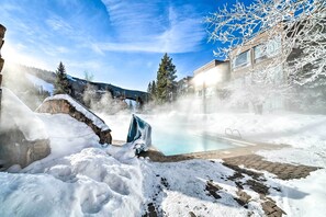 Ett snötäckt utomhusområde med en pool, stenmurar och en klar himmel.