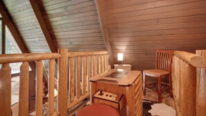 Interior de uma cabana de madeira com um banco, uma mesa pequena e uma cadeira de madeira.