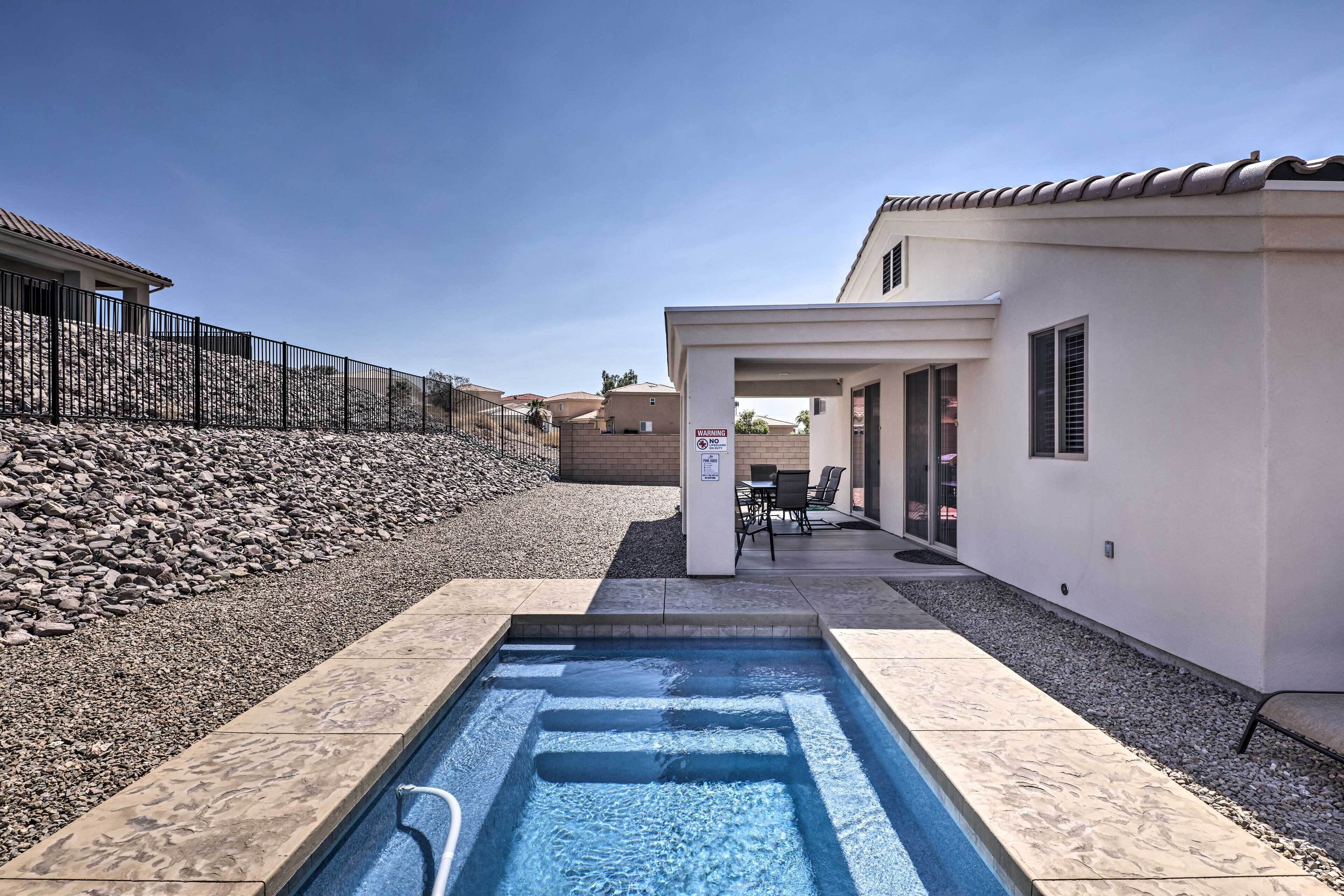 Una piscina con borde de piedra, un patio con mobiliario exterior y un edificio con tejado de azulejos.