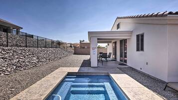 Una piscina con borde de piedra, un patio con mobiliario exterior y un edificio con tejado de azulejos.
