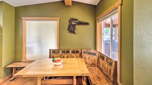A dining area with a wooden table and benches, a decorative bird headpiece on the wall, and a window with blinds. - Lakefront Eatonville Cabin w/ Dock & Mtn Views! (Eatonville)