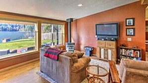 A living room with a large window, a fireplace, a television, and a bookshelf. - Lakefront Eatonville Cabin w/ Dock & Mtn Views! (Eatonville)