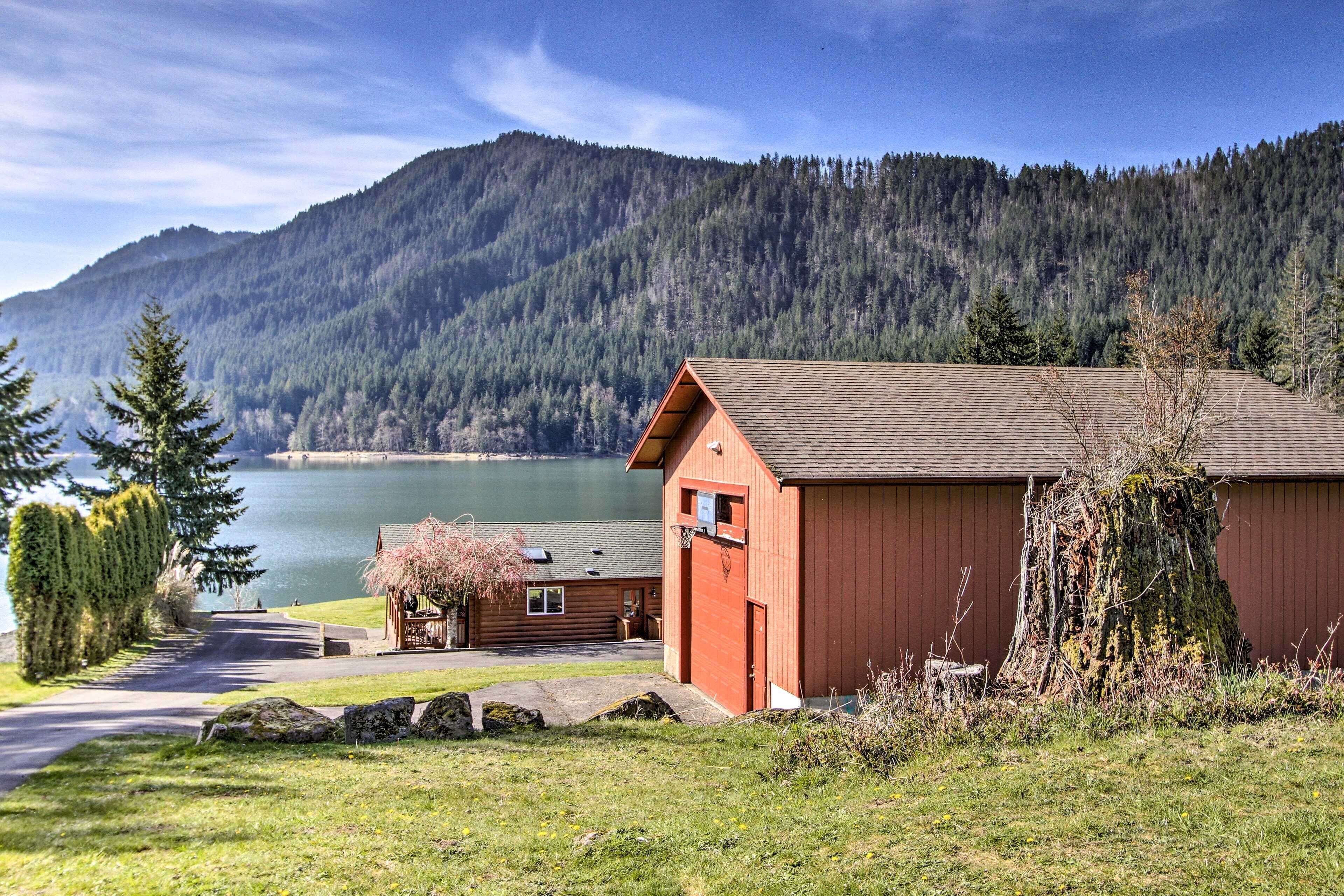 A cabin with a wooden exterior, a small porch, and a view of a lake and forested mountains.
