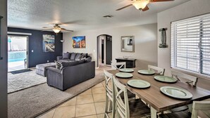 A modern living room with a dark gray sofa, a wooden dining table set with plates, and a ceiling fan. - Lake Havasu City Retreat w/ Patio & Grill (Lake Havasu City)