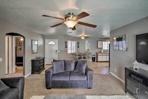 A living room with a gray sofa, a ceiling fan, a TV, and a dining area in the background. - Lake Havasu City Retreat w/ Patio & Grill (Lake Havasu City)